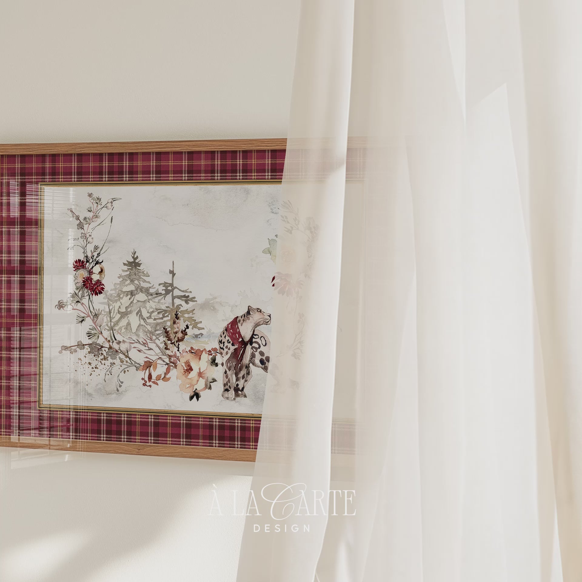 Printable Christmas wall art featuring a watercolor snow leopard in a red scarf, surrounded by snowy evergreen trees, winter flowers and branches, framed by a red tartan plaid border.